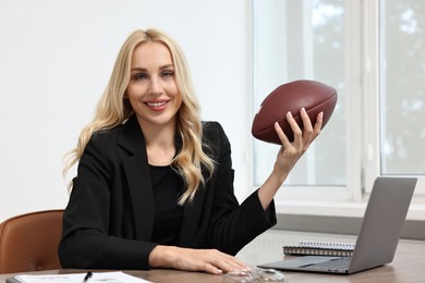 Happy woman with american football ball at table in office