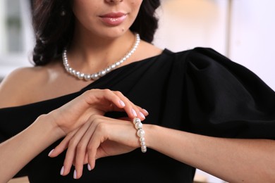 Young woman trying on elegant pearl bracelet indoors, closeup