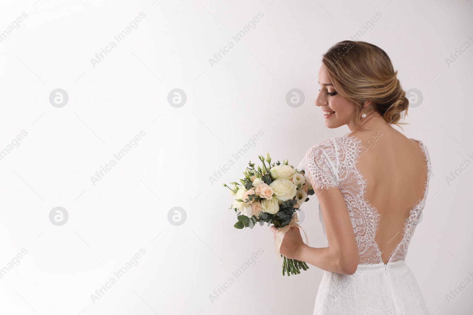 Photo of Young bride with elegant hairstyle holding wedding bouquet on white background, back view