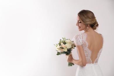 Photo of Young bride with elegant hairstyle holding wedding bouquet on white background, back view