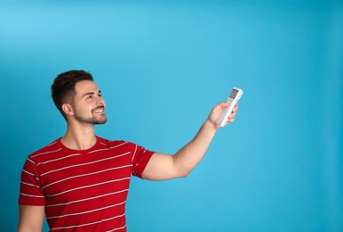 Photo of Happy young man operating air conditioner with remote control on light blue background. Space for text