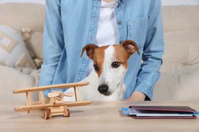 Photo of Woman with passport, toy plane and dog at wooden table indoors. Travel with pet concept