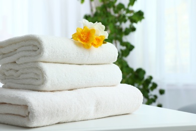 Photo of Stack of fresh towels with flowers on table indoors. Space for text