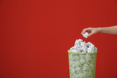 Photo of Woman throwing crumpled paper into metal bin against color background. Space for text