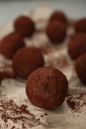 Photo of Delicious chocolate candies powdered with cocoa on parchment paper, closeup