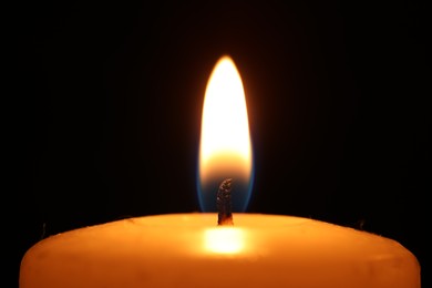 Burning wax candle on black background, closeup