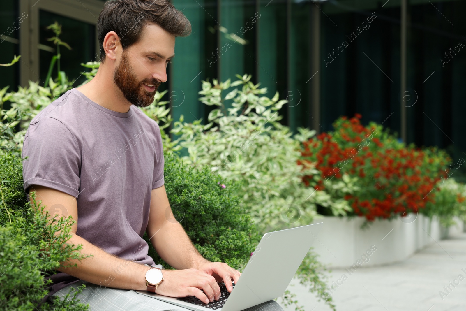 Photo of Handsome man with laptop near beautiful plants on city street