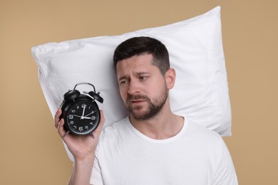Sleepy man with pillow and alarm clock on beige background. Insomnia problem