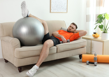 Photo of Lazy young man with sport equipment on sofa at home