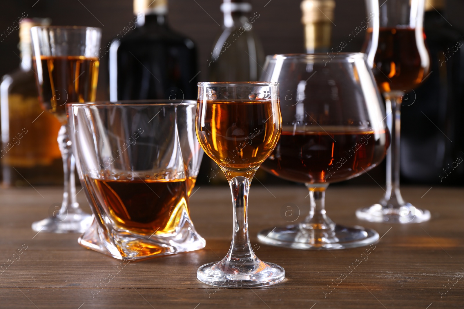 Photo of Different delicious liqueurs in glasses and bottles on wooden table