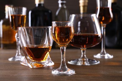 Photo of Different delicious liqueurs in glasses and bottles on wooden table
