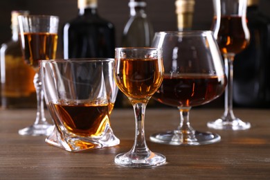 Different delicious liqueurs in glasses and bottles on wooden table