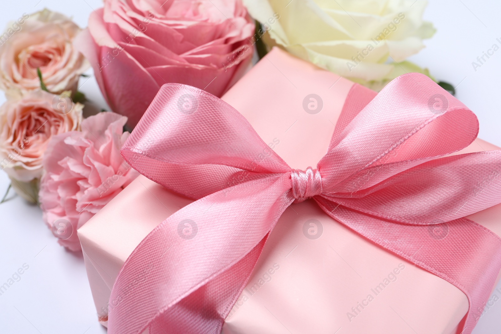 Photo of Gift box and beautiful flowers on white background, closeup