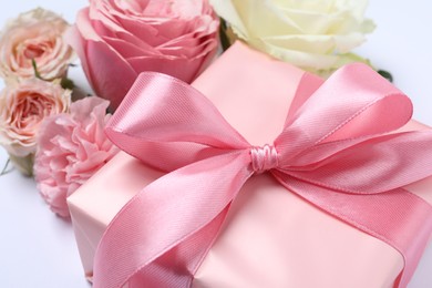 Gift box and beautiful flowers on white background, closeup