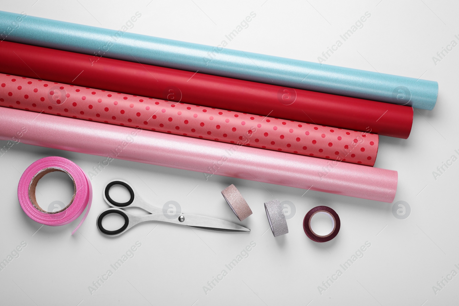 Photo of Rolls of colorful wrapping papers, scissors and ribbons on white background, flat lay