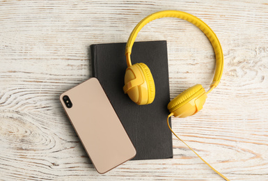 Book, modern headphones and smartphone on white wooden table, flat lay