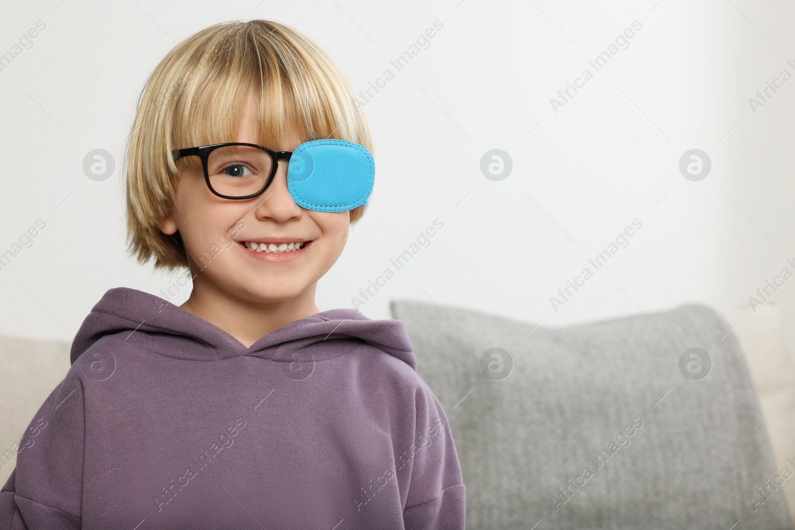 Photo of Happy boy with nozzle on glasses for treatment of strabismus in room. Space for text