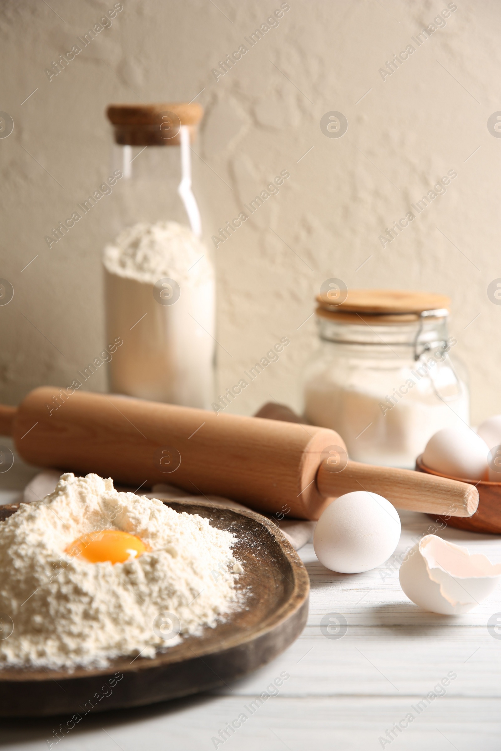 Photo of Making dough. Pile of flour with yolk, rolling pin and eggs on white wooden table, closeup