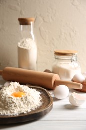 Photo of Making dough. Pile of flour with yolk, rolling pin and eggs on white wooden table, closeup