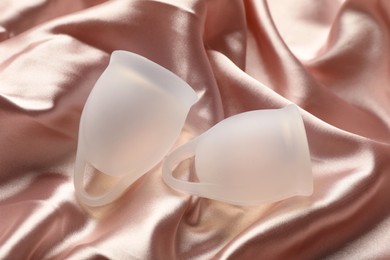 Photo of Menstrual cups on pink silk fabric, flat lay