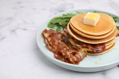 Tasty pancakes with butter, fried bacon and fresh arugula on white marble table. Space for text