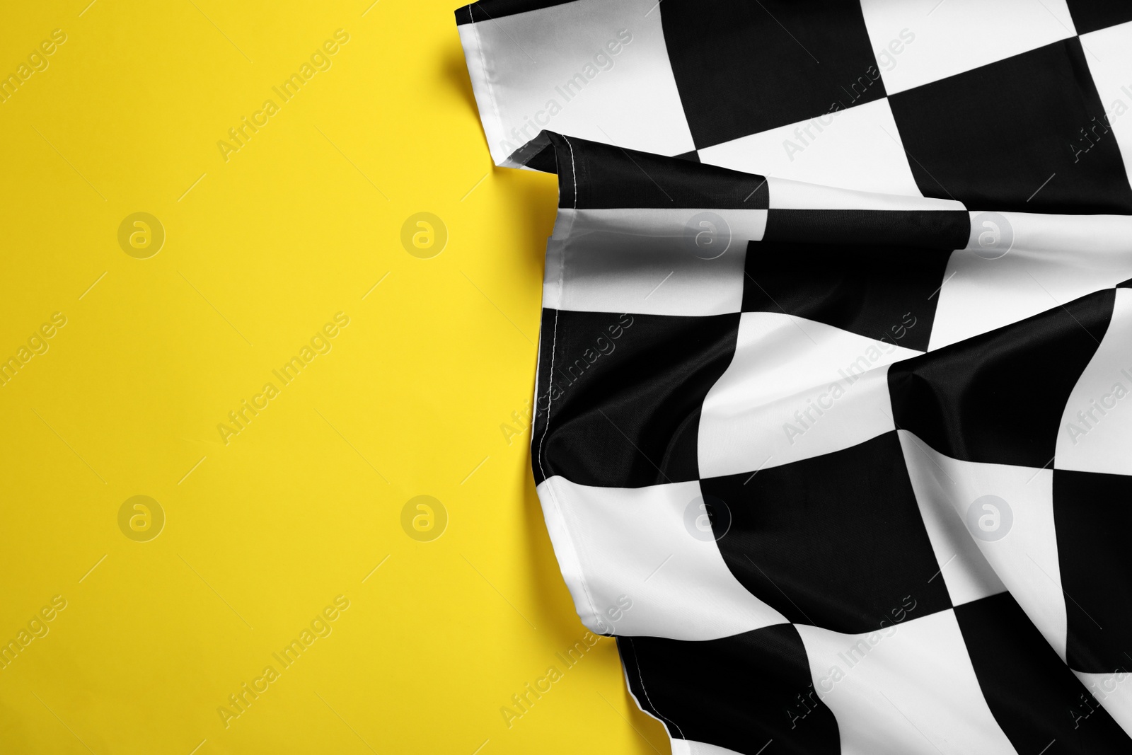 Photo of Checkered finish flag on yellow background, top view. Space for text