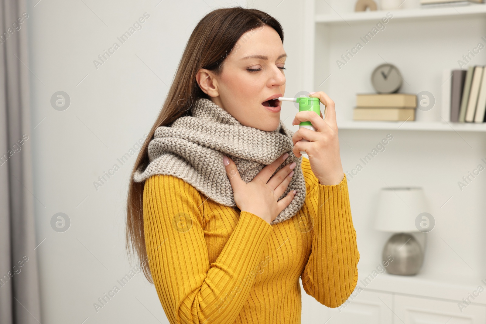 Photo of Adult woman with scarf using throat spray at home