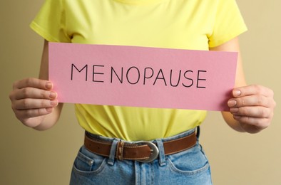 Photo of Woman holding card with word Menopause on beige background, closeup