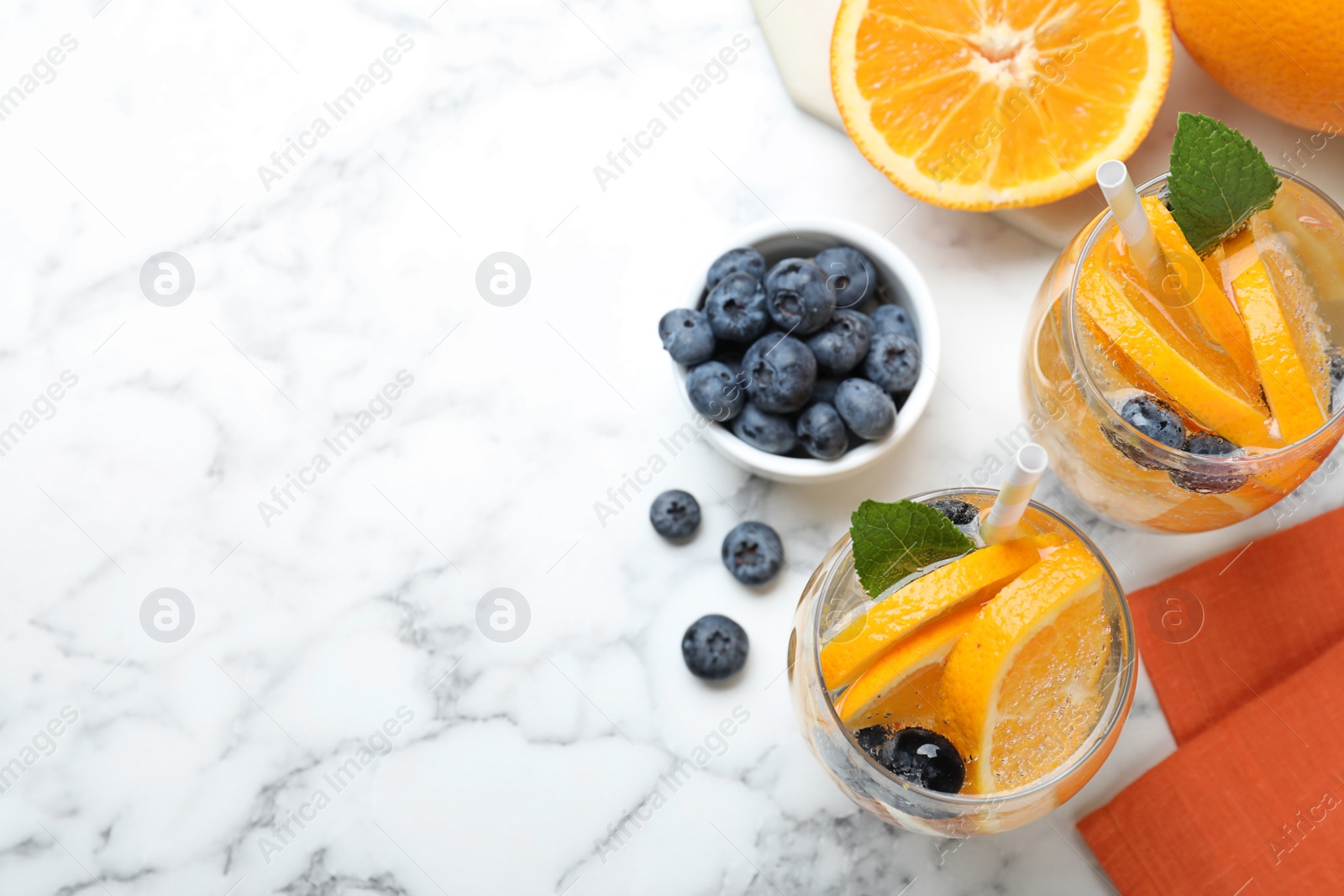 Photo of Flat lay composition of delicious orange lemonade with soda water, mint and blueberries on white marble table, space for text. Fresh summer cocktail