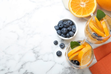 Flat lay composition of delicious orange lemonade with soda water, mint and blueberries on white marble table, space for text. Fresh summer cocktail