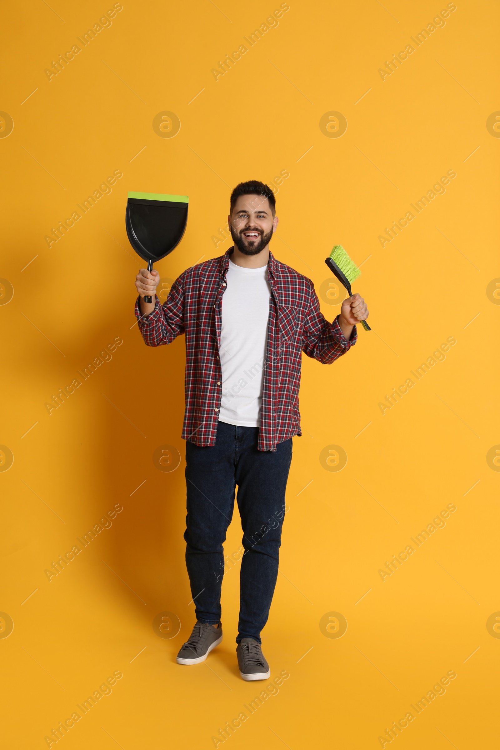 Photo of Young man with broom and dustpan on orange background