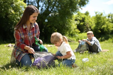 Mother and her children with plastic bags collecting garbage in park