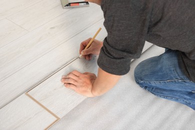 Photo of Professional worker using pencil during installationnew laminate flooring, closeup