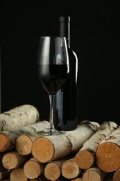 Red wine in wineglass and bottle on wooden logs against black background