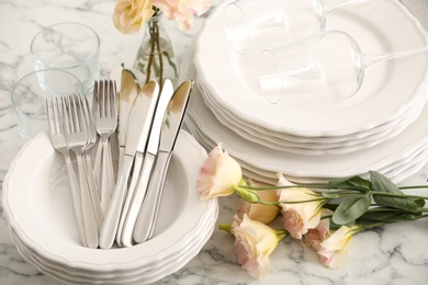 Photo of Stacked plates, cutlery and flowers on white marble table, closeup