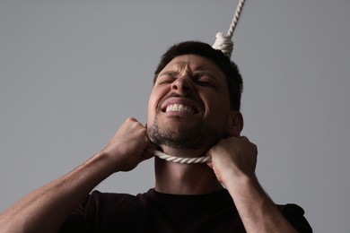 Photo of Depressed man with rope noose on neck against light grey background