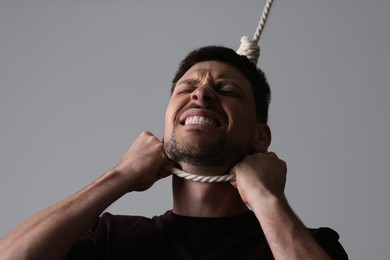 Depressed man with rope noose on neck against light grey background