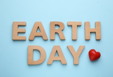 Photo of Phrase Earth Day made with wooden letters and red heart on light blue background, flat lay