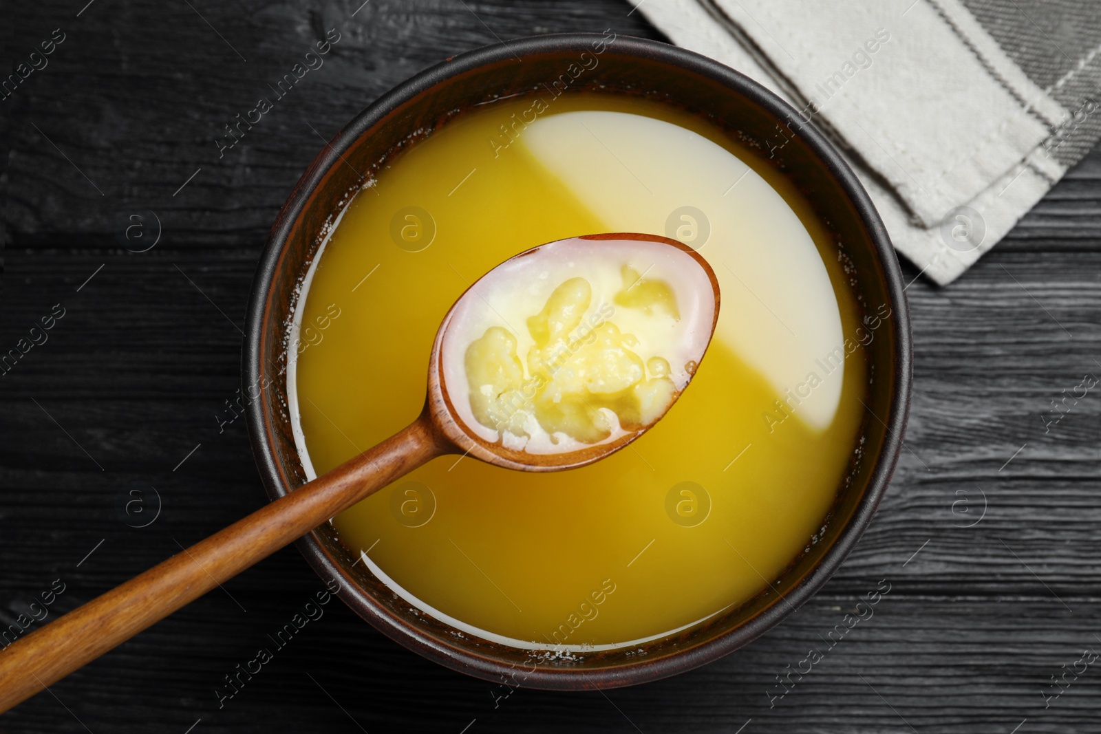 Photo of Bowl and spoon of Ghee butter on dark wooden table, flat lay