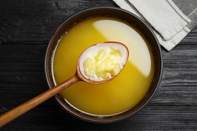 Photo of Bowl and spoon of Ghee butter on dark wooden table, flat lay