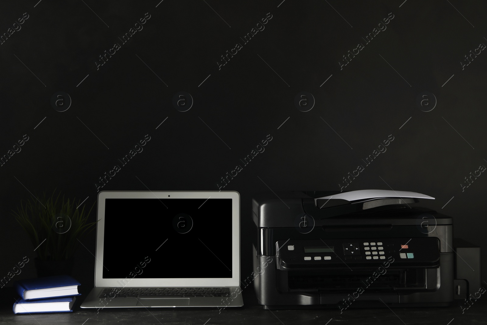 Photo of New modern printer, laptop and office supplies on black table