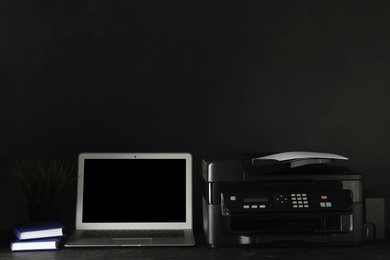 Photo of New modern printer, laptop and office supplies on black table