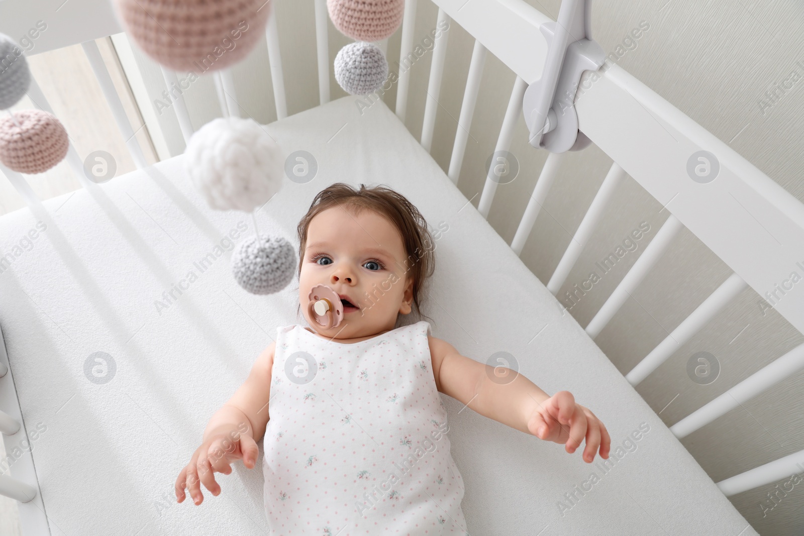 Photo of Cute little baby looking at hanging mobile in crib