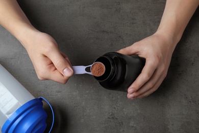 Man preparing protein shake with powder at grey table, top view