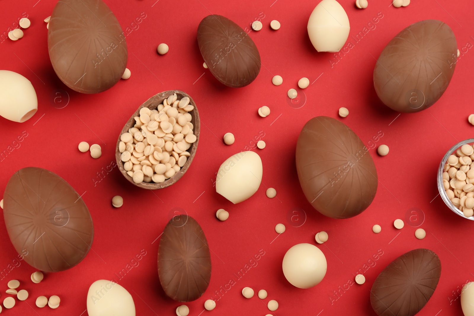 Photo of Sweet chocolate eggs and candies on red background, flat lay