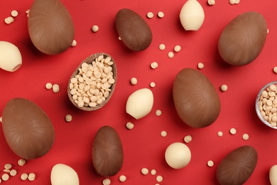 Photo of Sweet chocolate eggs and candies on red background, flat lay