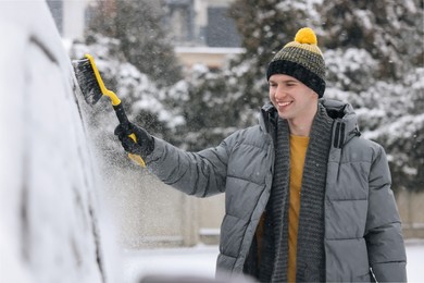 Photo of Man cleaning snow from car with brush outdoors