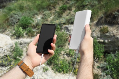 Photo of Man charging mobile phone with power bank on mountain hill, closeup