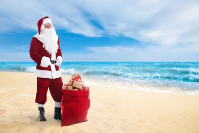 Image of Santa Claus and sack of gifts on beach near sea, space for text. Christmas vacation 