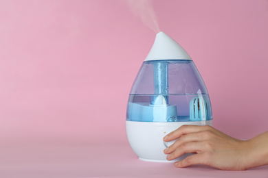 Woman using modern air humidifier on pink background, closeup. Space for text